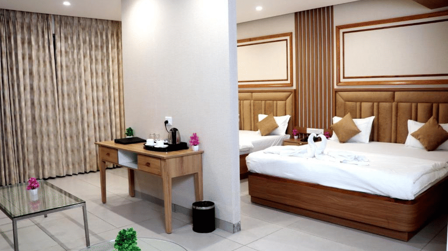 A Family Suite at the Prince ZENQ Xpress Resortt Rohtak featuring a main bedroom area with two large beds separated by a half-wall from a small living area with a console table and glass coffee tables.