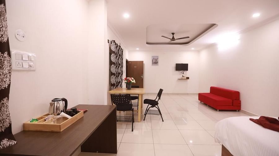 A full view of room with a red sofa, work desk, and a plush bed. | Vistar Resort, Bengaluru