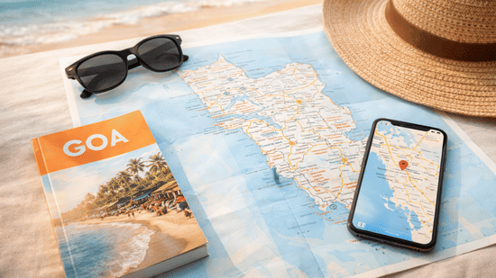 A map, a phone, sunhat and sunglasses resting on the sand.