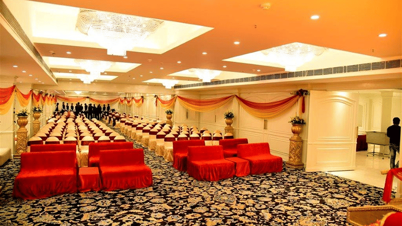 An elegant  banquet hall, with ornate golden ceiling details, red velvet seating, patterned carpeting, and opulent interior design at a luxury hotel in Lucknow - Clarks Avadh, Lucknow.