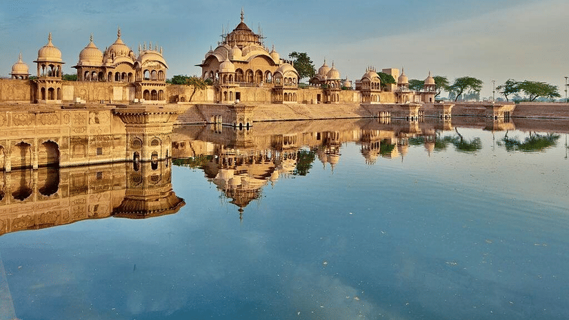 Historic temple structures reflected in the calm waters at a scenic ghat in Mathura-Vrindavan during sunrise.