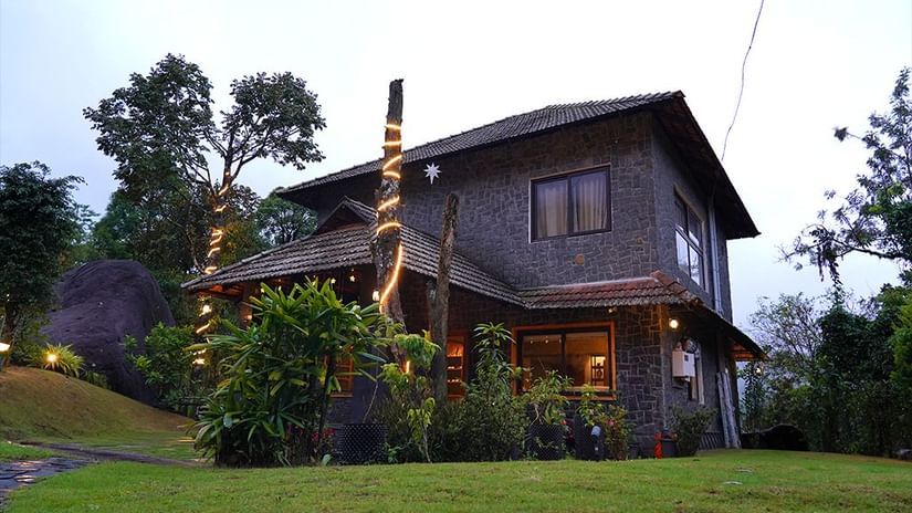 A cosy wooden cottage with warm lighting, surrounded by greenery and trees in a serene natural setting at  The Wild Trails Clarks Exotica, Munnar.