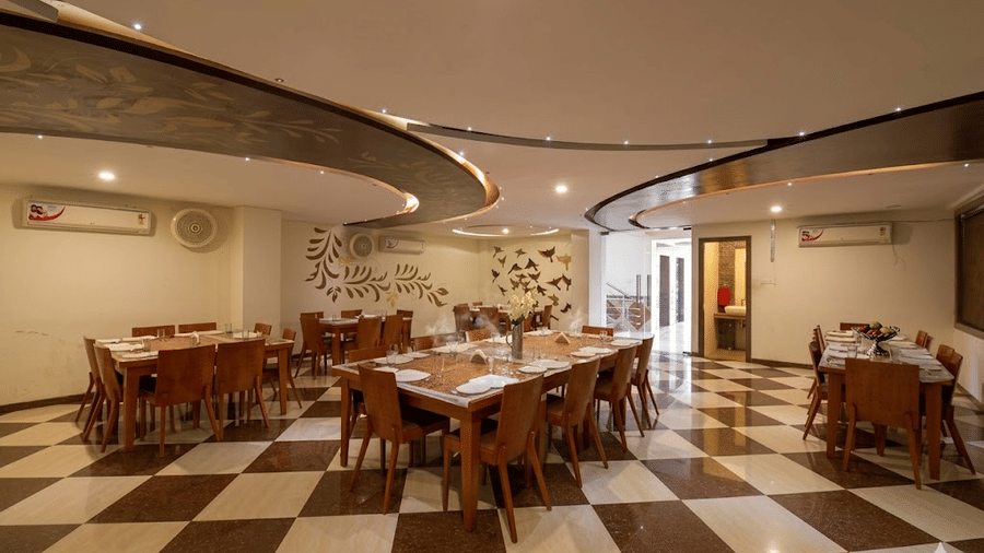 Wide angle view of a dining hall with checkered tile floors, multiple wooden tables, and structured curved ceilings.
