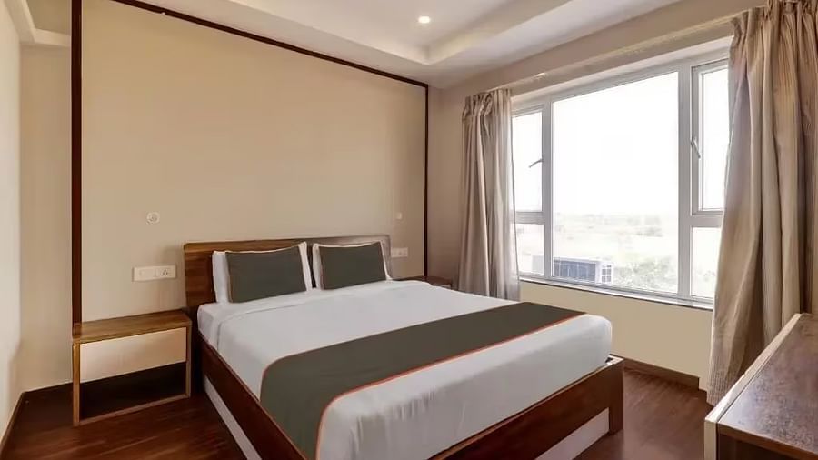 A hotel room with a double bed, dark headboard, and large window with light curtains - VITS Select Kailash Inn, Bagalkot