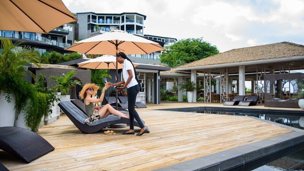 People relaxing on lounge chairs as a waiter serves them a drink.