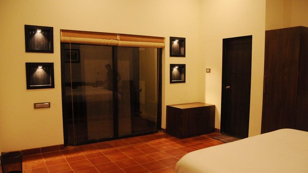 A bedroom with a sliding glass door, dark wood furniture, recessed picture frames, and a white bed.