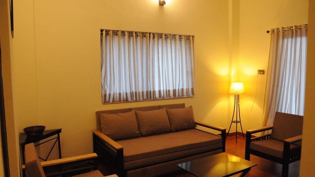 Beige sofa in a living room with a partial view of a kitchen through a wooden doorway.