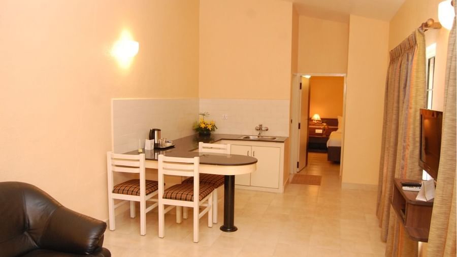 Living and dining area of the Deluxe Suite Room at Green Pastures Kodaikanal displaying a dining table, chairs, and a spacious layout with warm ambient lighting.