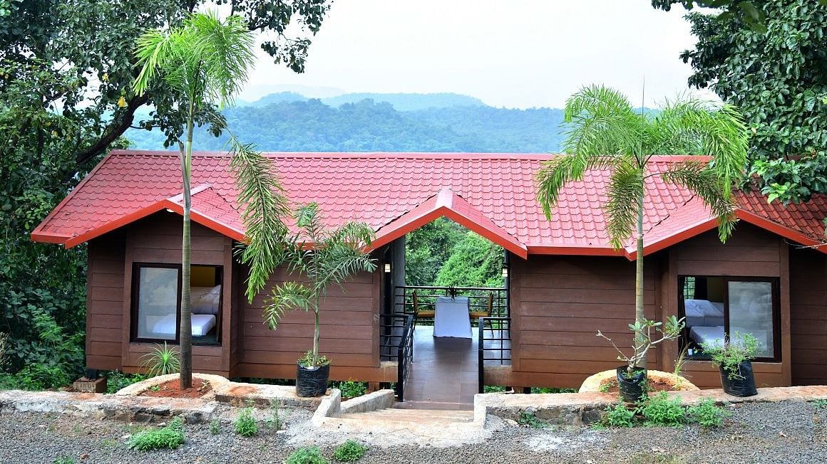 Riverview Luxury Cabin Exterior - Twin red-roofed wooden cabins in a forest setting with a mountain backdrop.