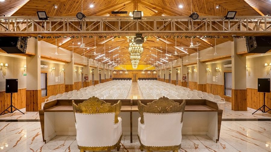 A large banquet hall with a stage area, speakers, and seating at the rear of Angel Lords Eco Inn Amreli.