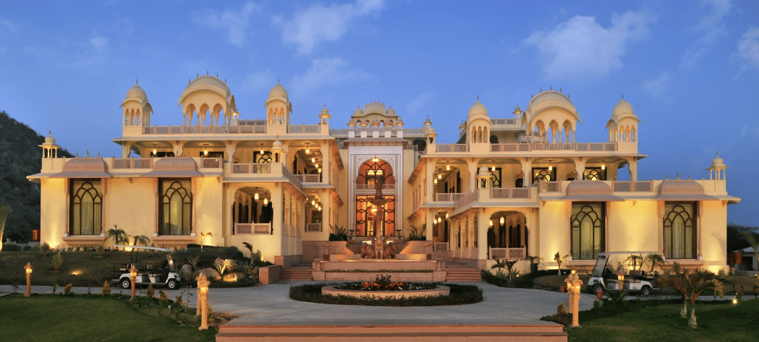 Facade of Rajasthali Resort & Spa Jaipur with plants in front and a clear sky in the background.