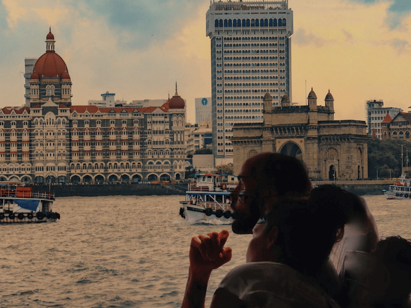 A tourist sitting on a ferry boat overlooking the heritage Taj Mahal Palace Hotel in Mumbai with the sea in the foreground during the evening hours.