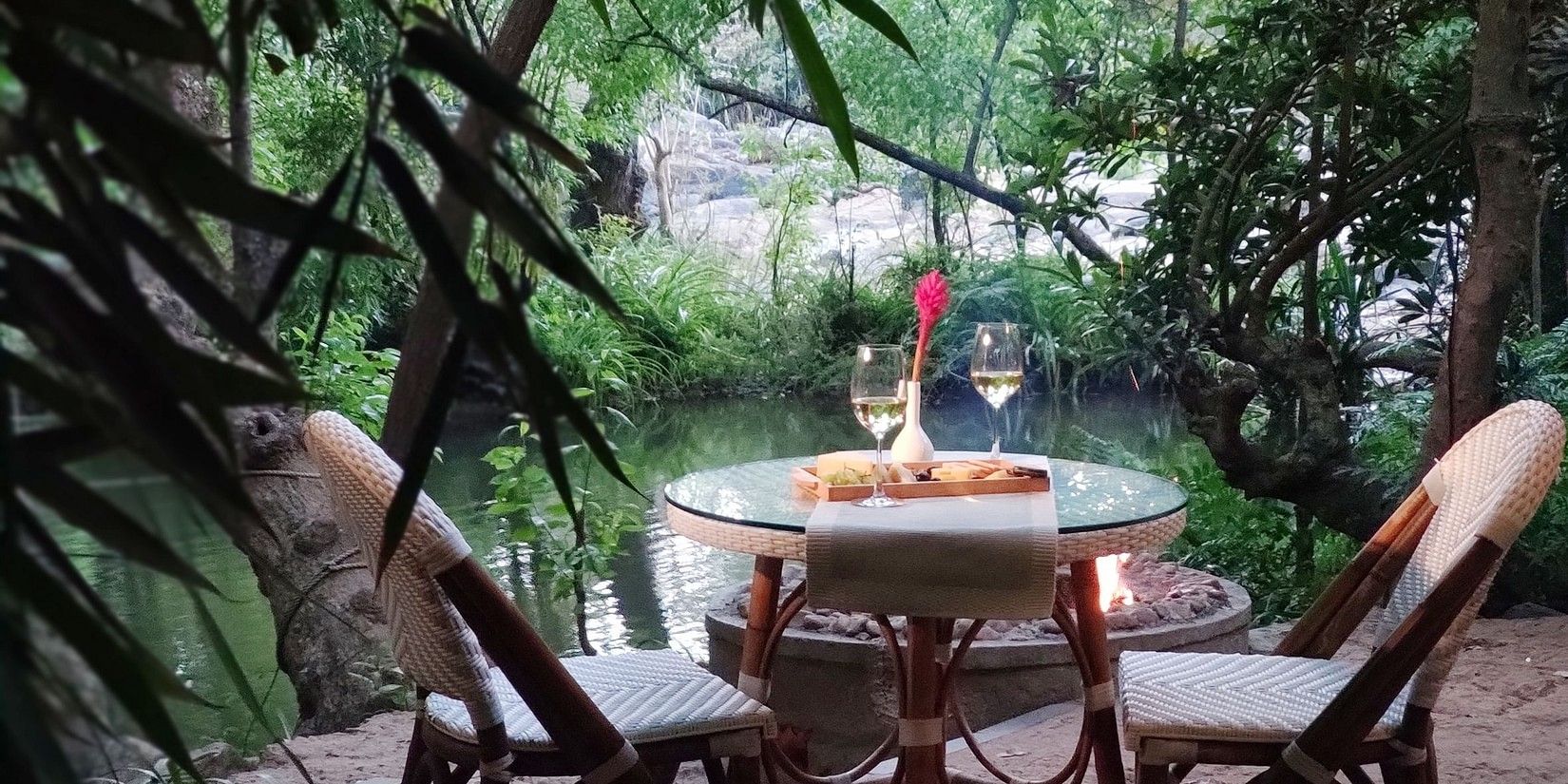 Outdoor dining setup by a river at dusk-Amanvana Spa Resort, Coorg - Luxury Resort