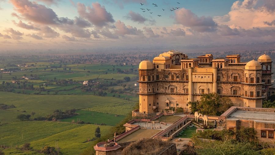 Face view of Rani Mahal perched on a hill at Tijara Fort-Palace - 19th Century, Alwar with green landscape and colourful sky in the background.