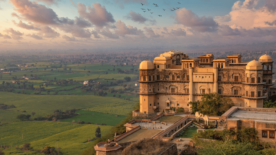Face view of Rani Mahal perched on a hill at Tijara Fort-Palace - 19th Century, Alwar with green landscape and colourful sky in the background - Tijara Resort