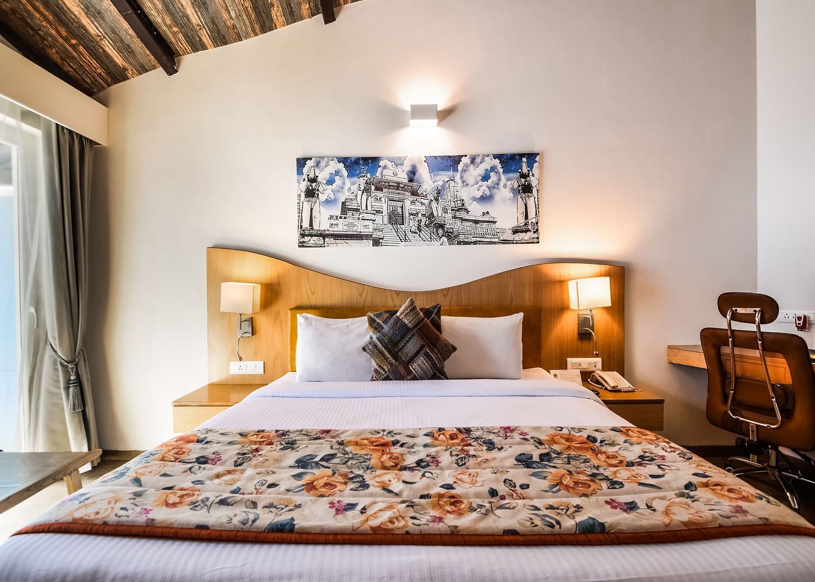 A bright room with a bed featuring a floral patterned runner, a desk, and a unique ceiling design. - Bamboo Saa Resort & Spa, Udaipur