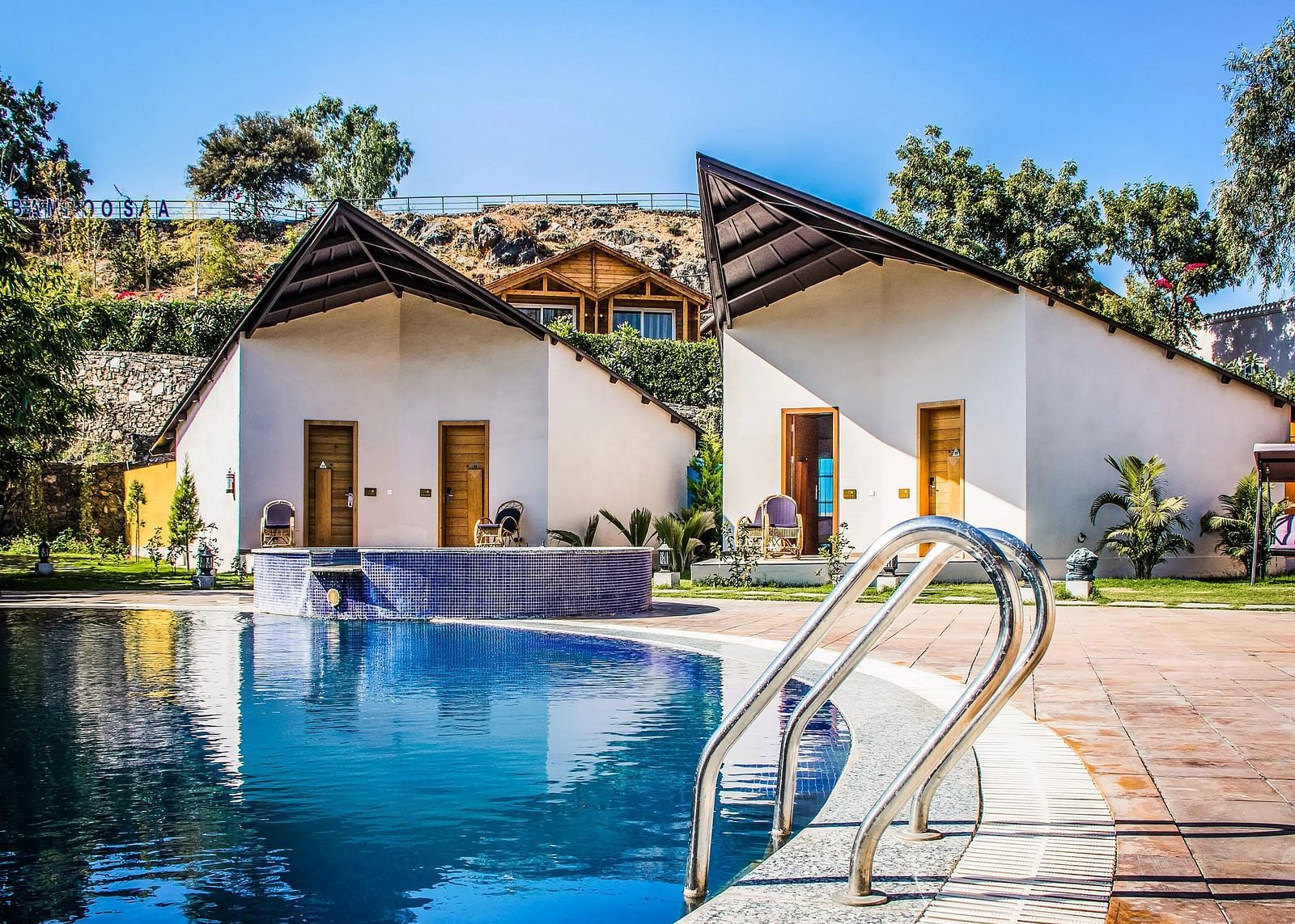 Two modern bungalows with pointed roofs flank a swimming pool.