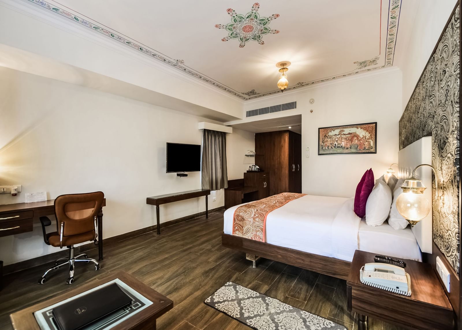  A hotel room with a large bed, a desk, and a seating area with warm lighting.- Bamboo Saa Resort & Spa, Udaipur