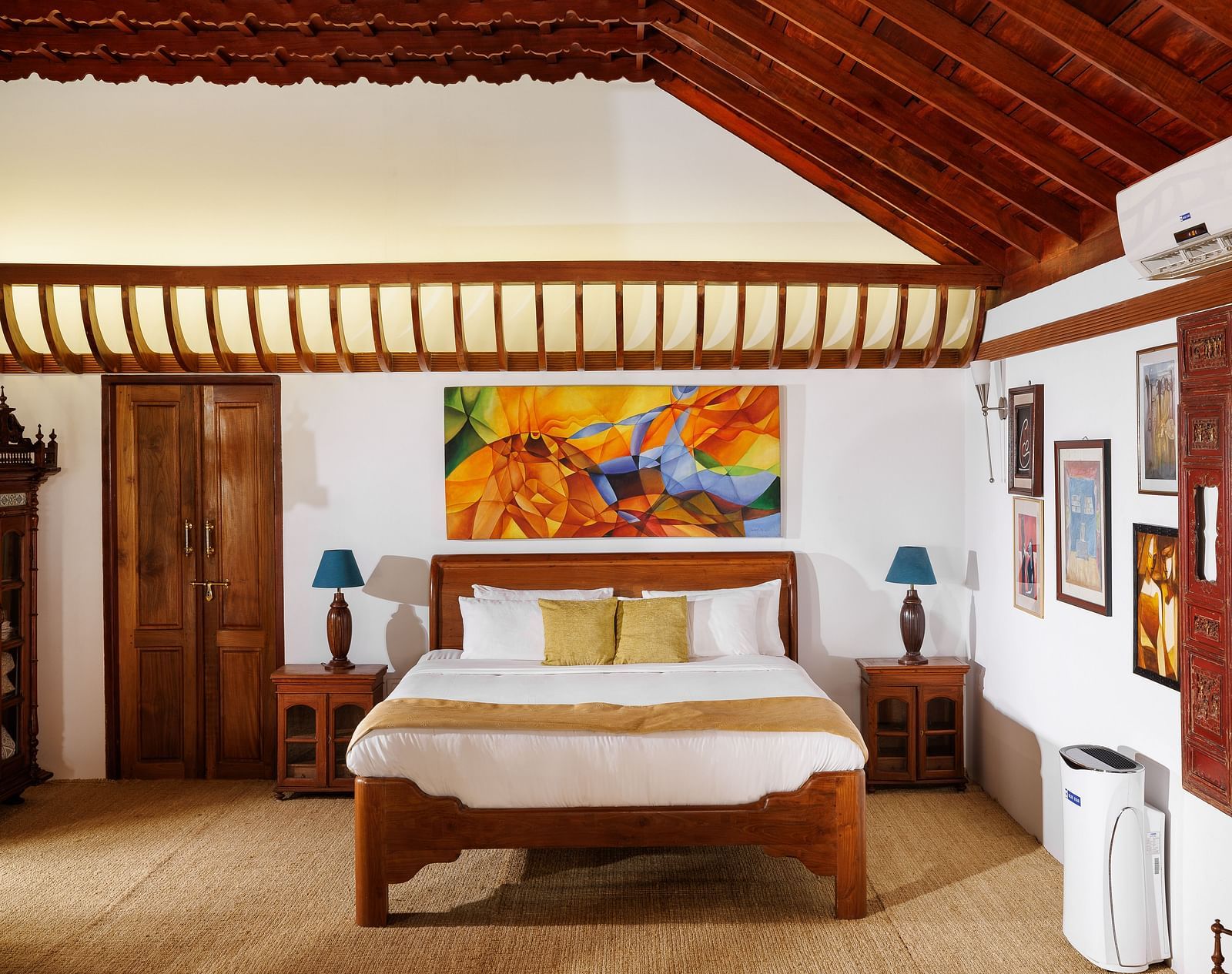 A room with wooden interiors featuring a bed, bedside tables, and paintings hung on the wall - BluSalzz Villas - Muhamma Resort, Alleppey