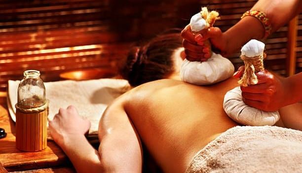 A person receives a relaxing herbal compress massage, lying face down on a spa bed with soothing ambience - Ocean Spray Puducherry 