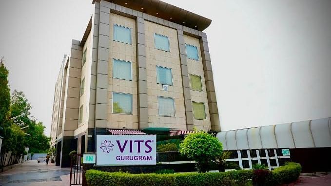 A low-angle exterior shot of a multi-storey building with a sign that reads VITS GURUGRAM, surrounded by greenery