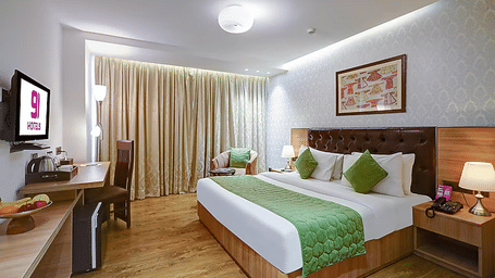 A spacious guest room with hardwood floors, floor-to-ceiling drapes, and a comfortable bed setup with green decorative pillows - Hotel 91 HUDA City Centre, Gurugram