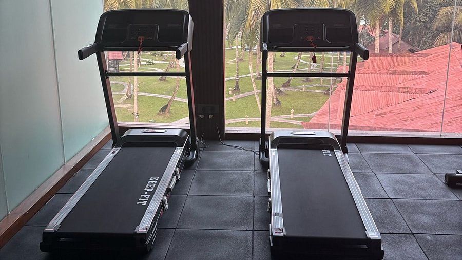Two treadmills facing a large window with a scenic view of palm trees and a red-roofed building outside - Silver Sand Beach Resort, Havelock.