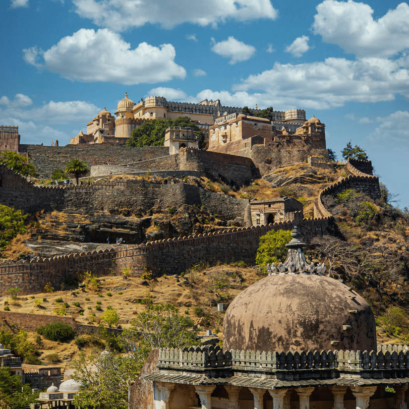 Hilltop view of Kumbhalgarh Fort with stone walls, domed structures, and the Aravalli Hills in the background
