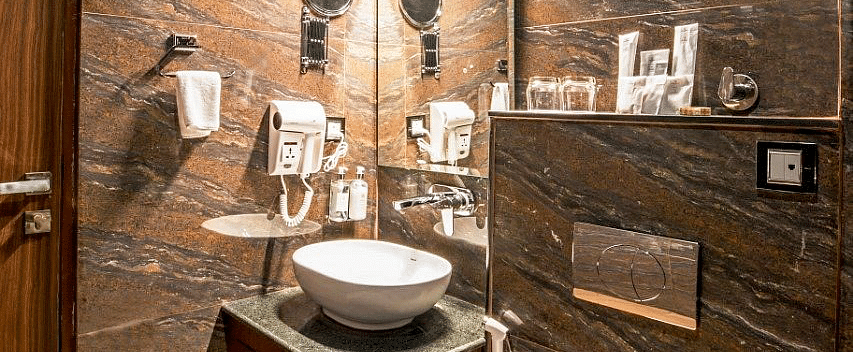 A bathroom with brown gradient tiles featuring a vanity area along with a commode besides it at Regenta Inn DLS.