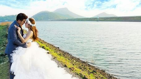 a bride and groom posing for a picture next to a waterbody with a mountain in the background