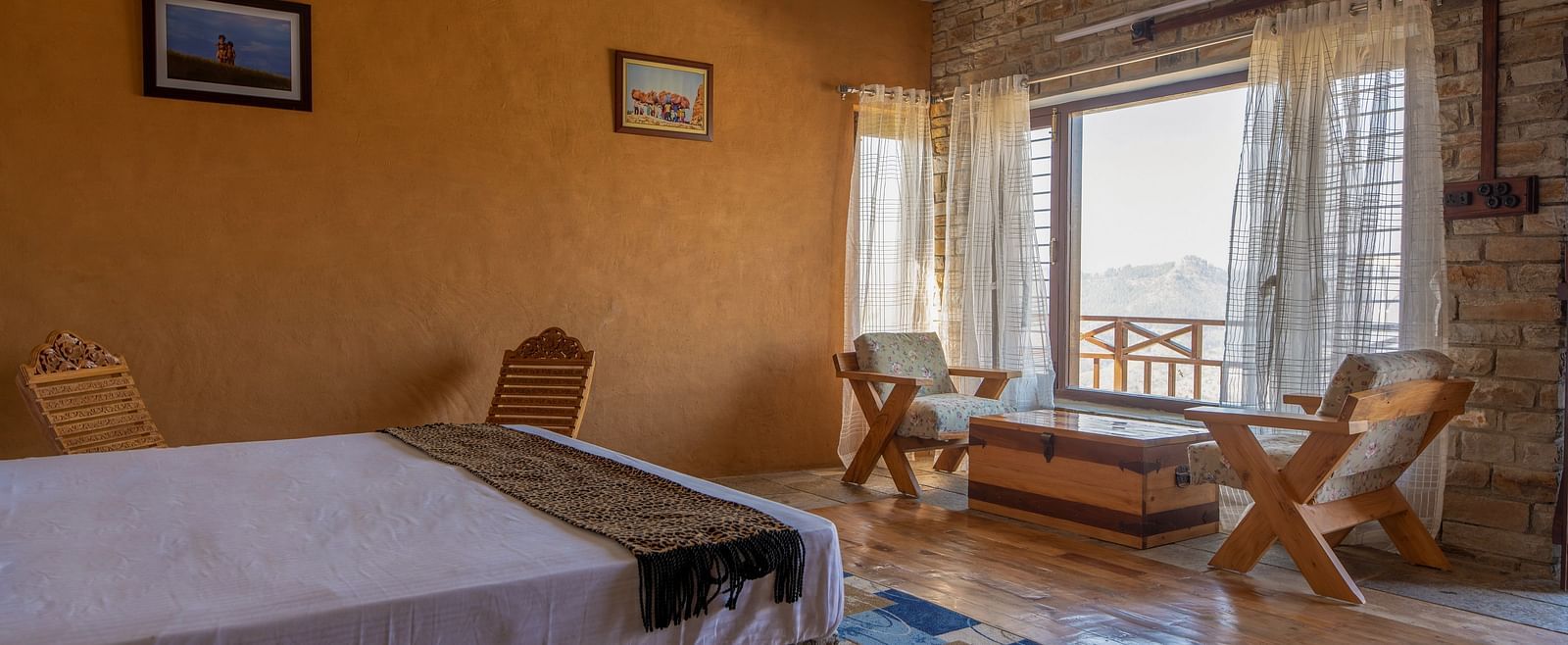 Rustic room with a bed, wooden chairs, stone wall, and a window with a mountain view. - Blusalzz Homes The Himalayan Bungalow, Almora