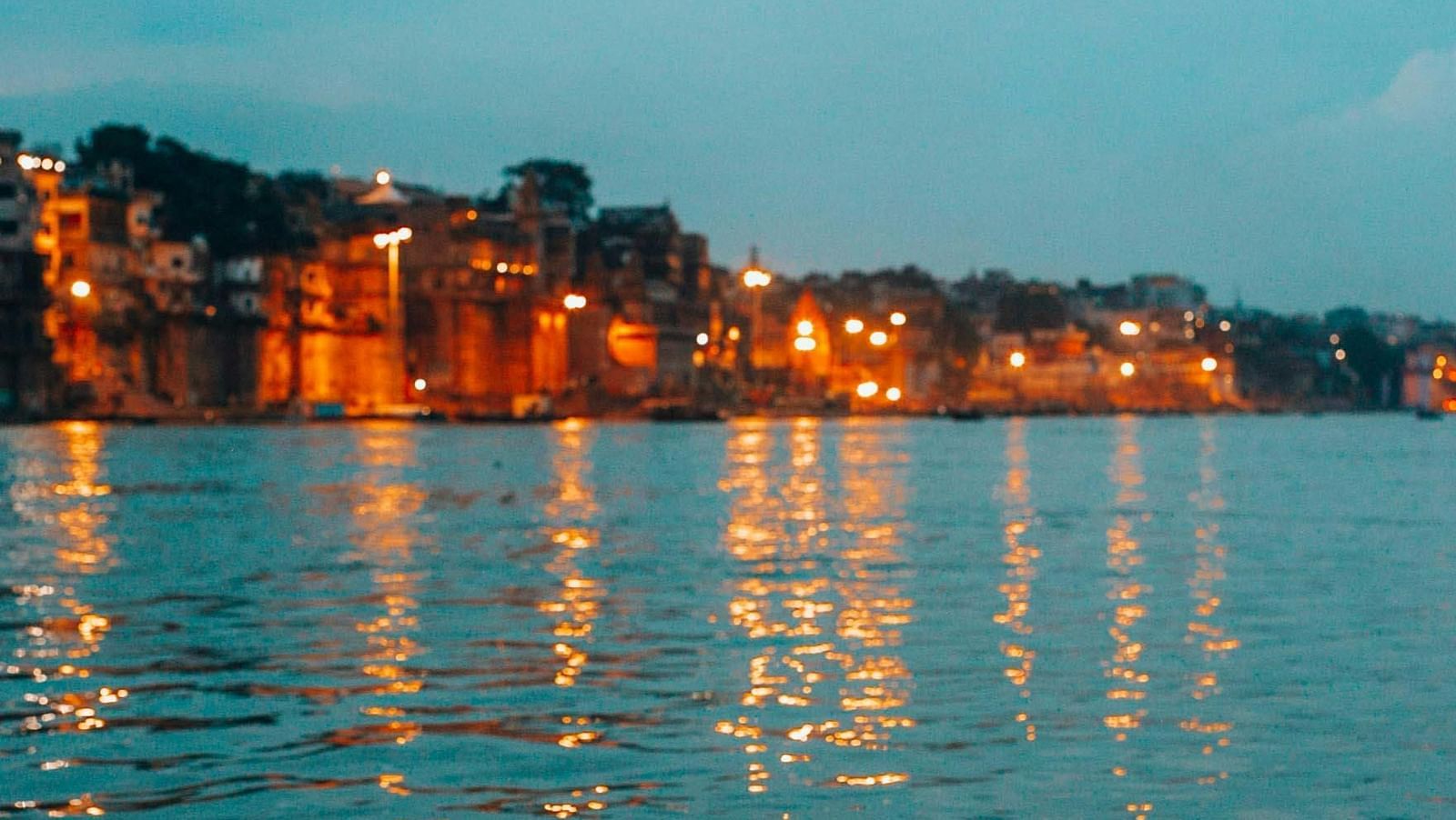 Riverside view of a town at dusk with glowing reflections on the water.