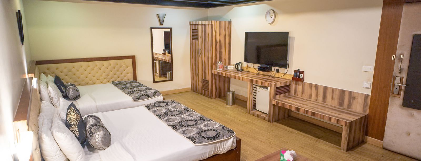 Family Room featuring two beds, a wooden bench, a small table, and a television.- Hotel Ashok Nagpur