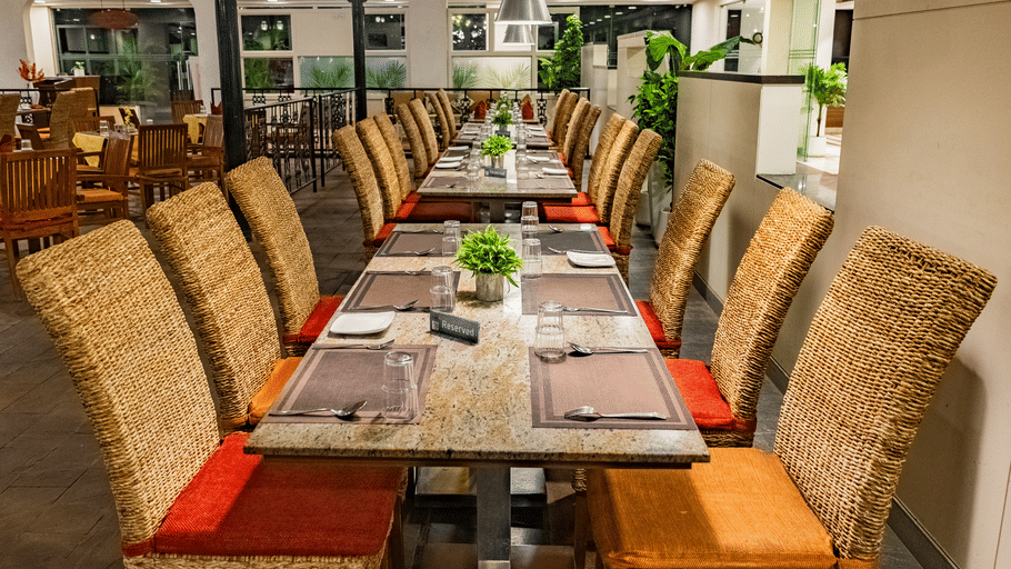 The Courtyard Restaurant at Featherlite Evoma Hotel with a long dining table, wicker chairs and pendant lights hanging overhead nearby.