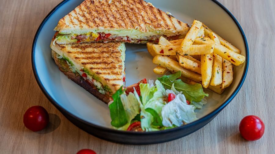 A plate with two triangular slices of sandwiches, accompanied by vegetables on the side, along with a pile of fries and mini tomatoes placed beside the plate at Indie Stays Mumbai International Airport.