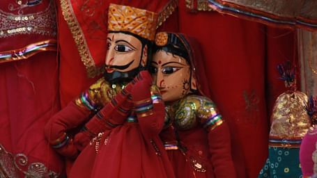 Rajasthani puppets, dressed in traditional attire with intricate details, are displayed against a backdrop of vibrant fabrics.