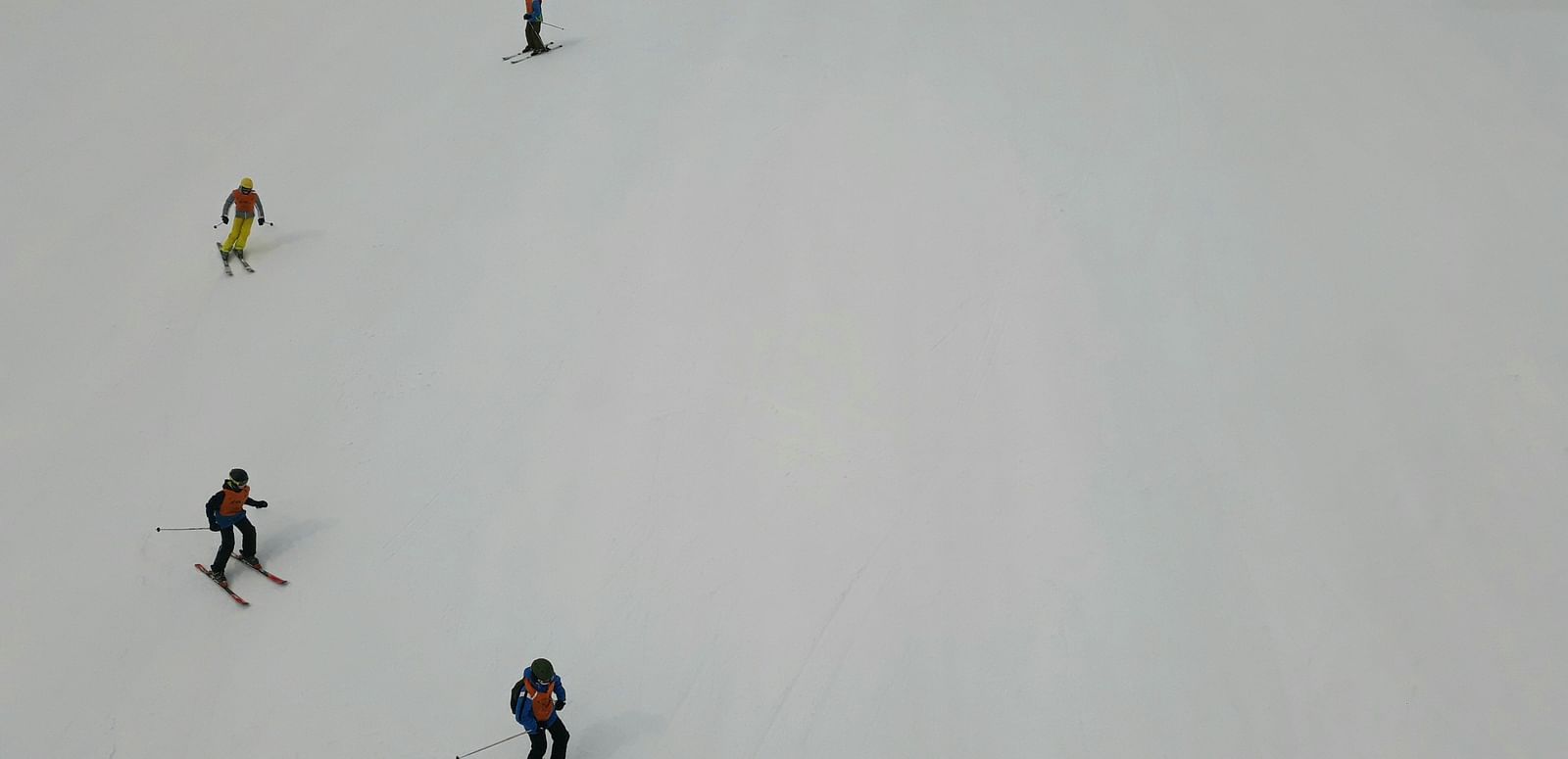 Skiers scattered across a snowy slope, seen from above.