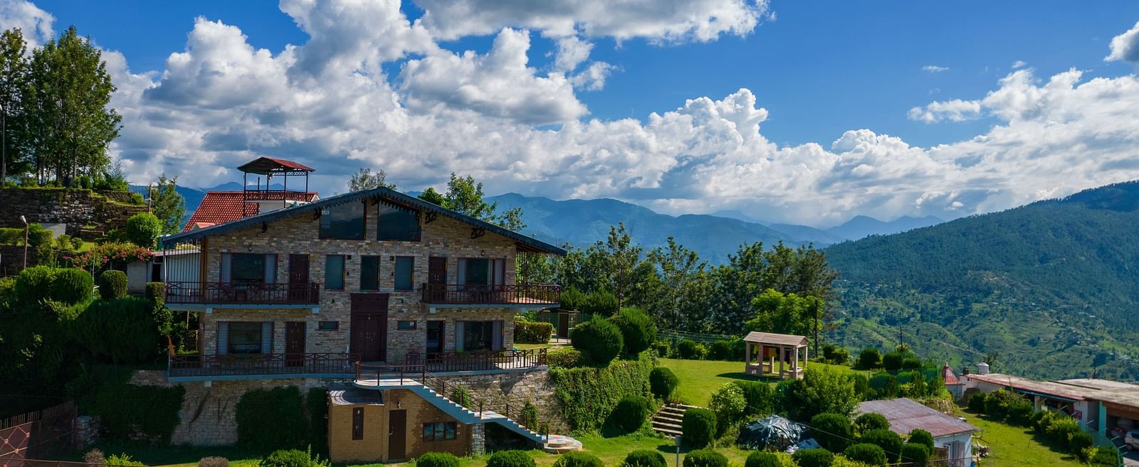 A charming villa surrounded by lush greenery and set against the backdrop of rolling hills and blue skies. - Blusalzz Homes The Himalayan Bungalow, Almora