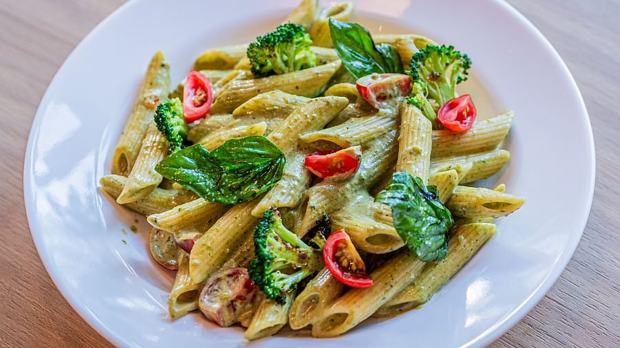 A plate of pasta topped with fresh vegetables, elegantly plated on a wooden surface at Indie Stays Mumbai International Airport.