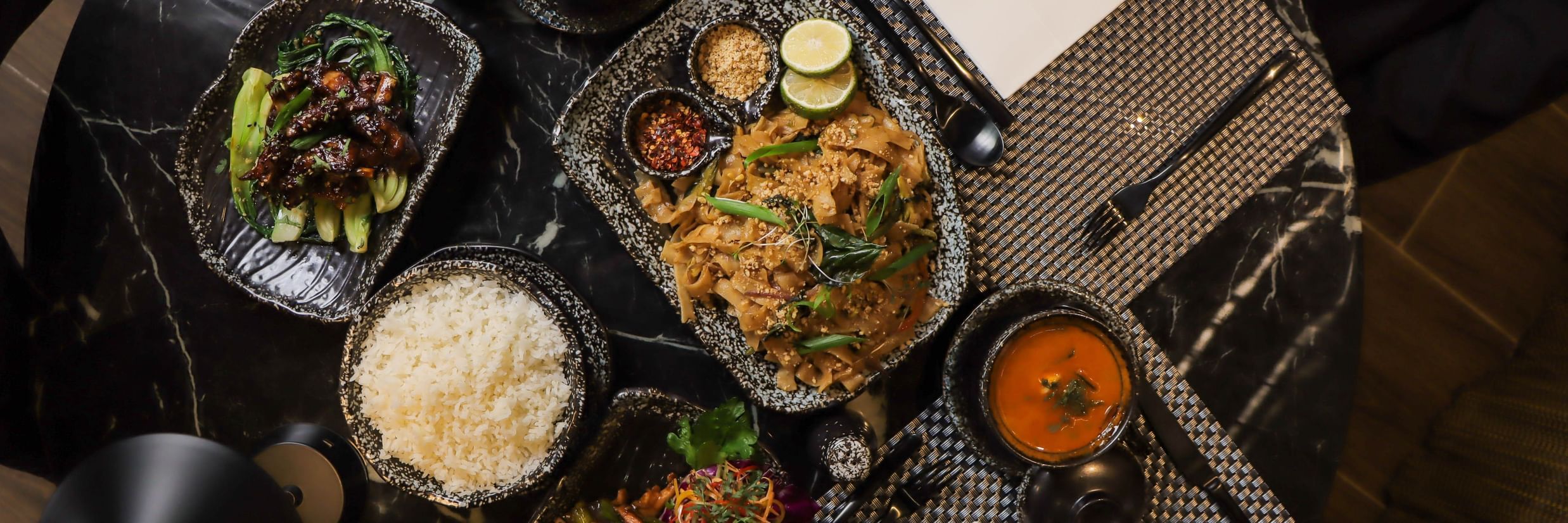 Table spread with plates and bowls containing rice, vegetables, curries, and sauces at Asiatic Lounge.