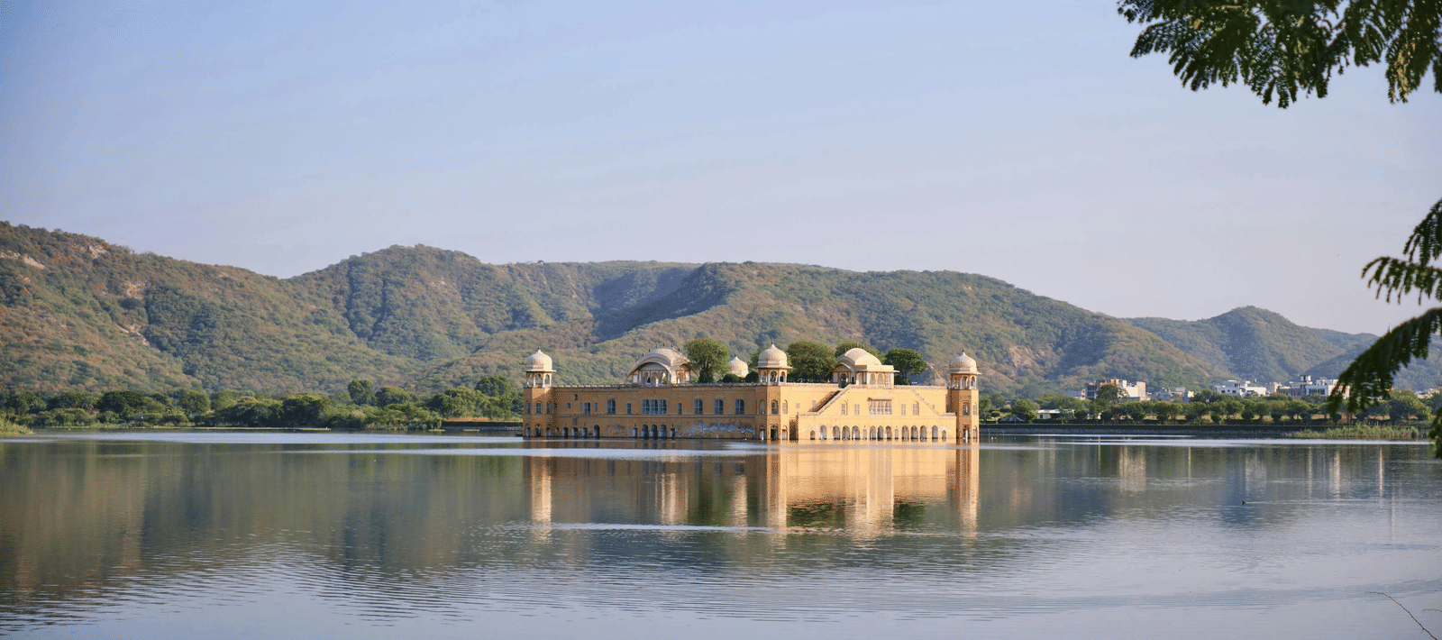 A small fortress situated in the middle of Fateh Sagar Lake in Udaipur, with lush green mountain ranges in the background.