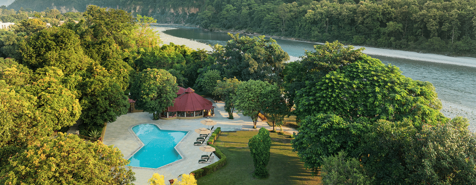 Panoramic view of The Riverview Retreat, Corbett, showing the swimming pool, lush grounds, and the Kosi River surrounded by hills.