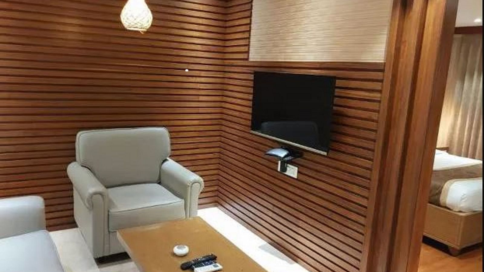 A section of a modern suite, featuring a cosy seating area with a grey sofa and a wooden coffee table, stylish shelving, and elegant lighting at Yashshree The Imperial Inn, Siliguri.