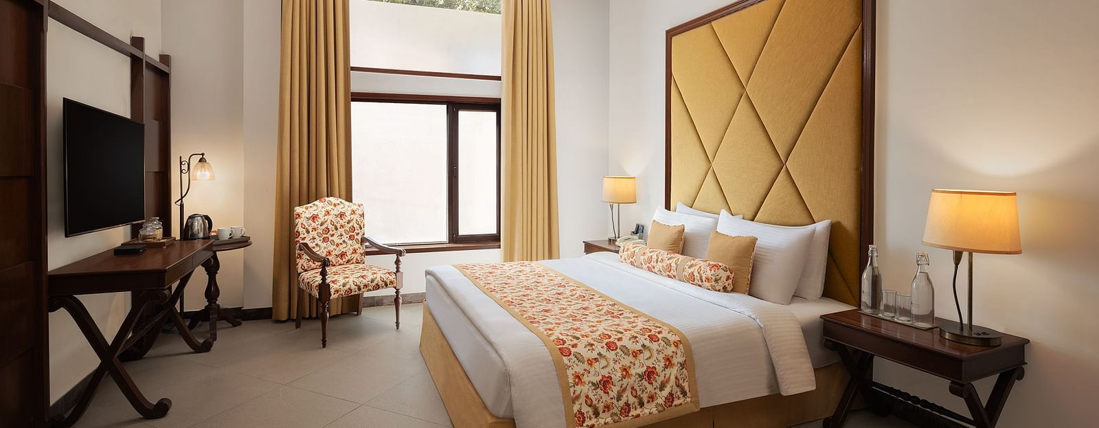 An image of a  cozy room in the naini retreat, nainital, with a double bed, wooden furniture, and a window. The room also features a ceiling fan, a TV .