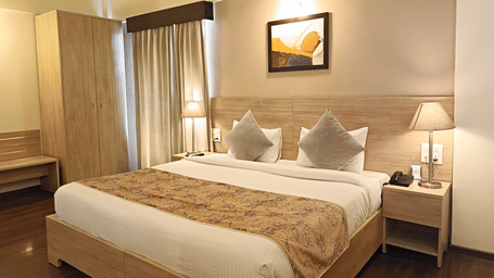 A plush bed with lamps lit on both sides on the nightstands inside a warmly lit Premium Room at Starlit Suites, Shirdi.