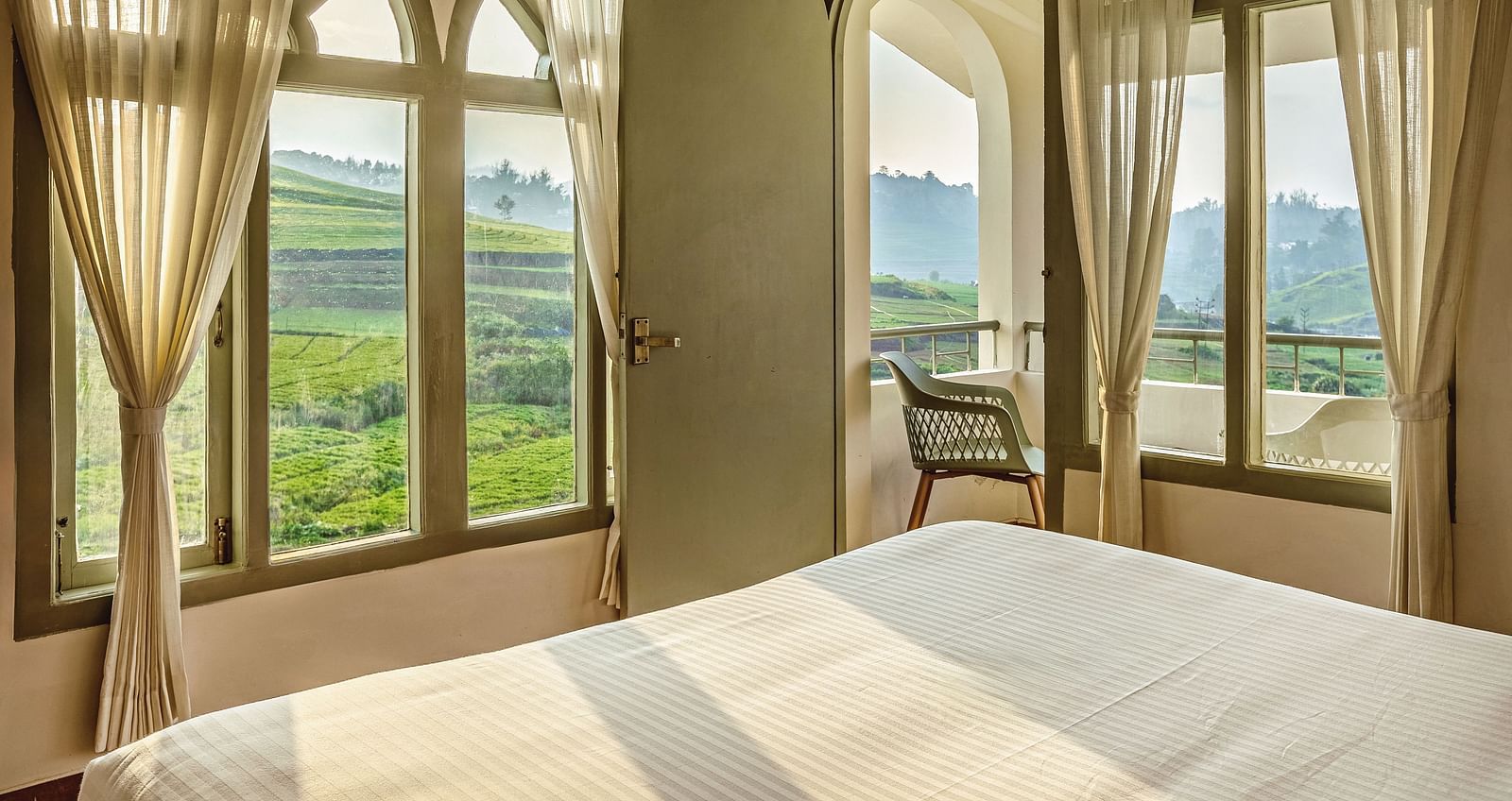 Bedroom at Mango Hill Shola, Ooty, featuring a large arched window with a scenic view of the surrounding landscape.