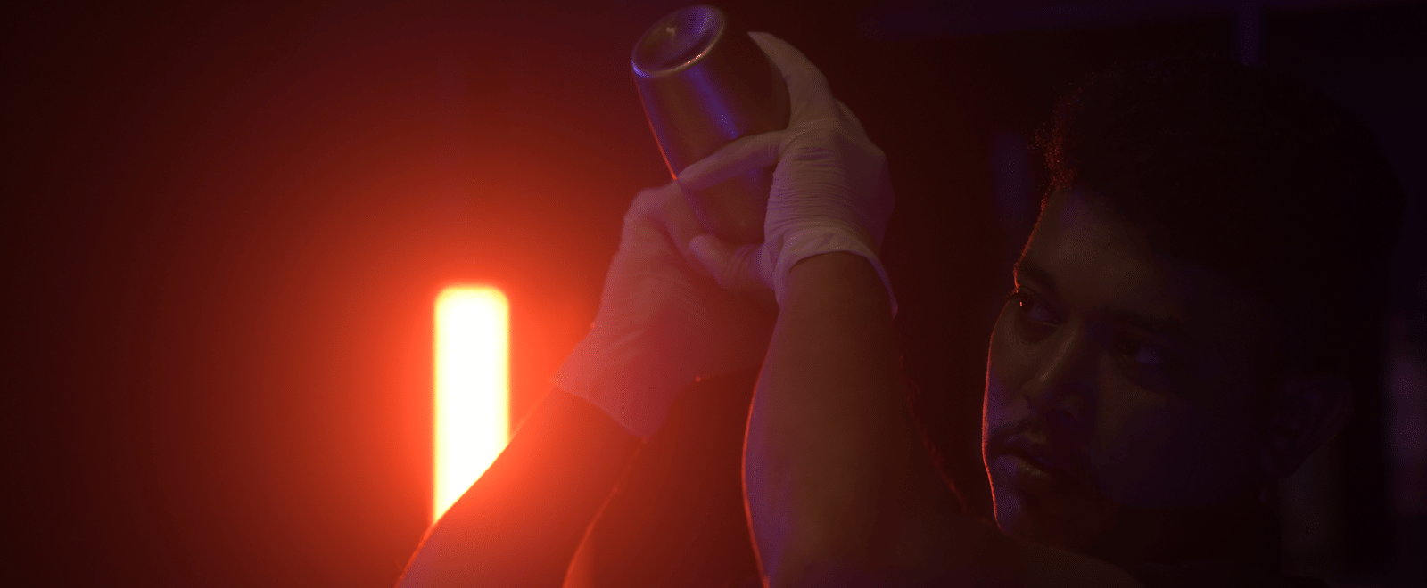 A bartender shaking a cocktail under soft red lighting, creating a warm and dramatic ambience at Hotel Sonar Bangla Mayapur.