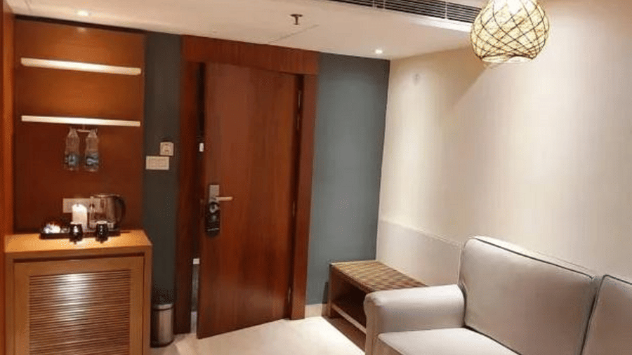 Living room with wooden panelling, a cosy armchair, a wooden coffee table with a cup, and a wall-mounted TV at Yashshree The Imperial Inn, Siliguri