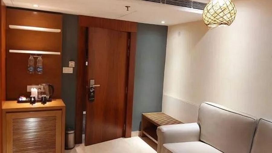 Living room of a suite with wooden panelling, a cosy grey armchair, a wooden coffee table with a cup, and a wall-mounted TV at Yashshree The Imperial Inn, Siliguri.