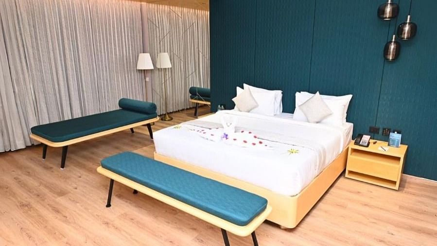A bedroom in Dhanalakshmi Srinivasan Hotels, Perambalur, with a large bed, two lounge chairs, and two armchairs. The room features wooden flooring and a dark blue accent wall.